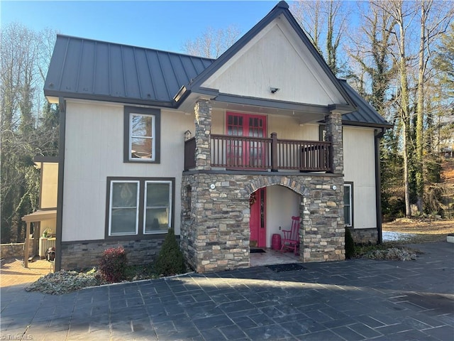 view of front of property with stone siding, a standing seam roof, metal roof, and a balcony