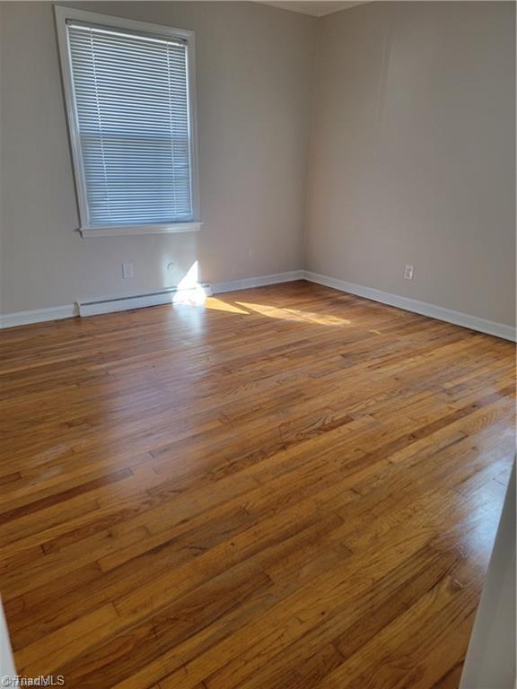 spare room featuring a baseboard radiator, wood finished floors, and baseboards