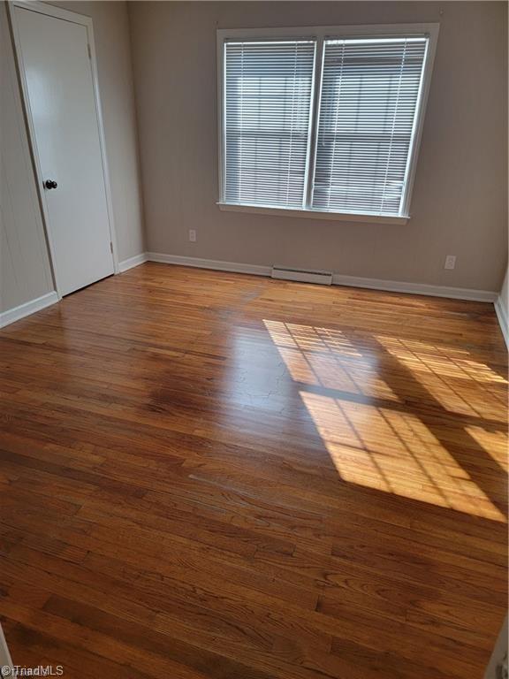 unfurnished room featuring a baseboard heating unit, baseboards, and wood finished floors