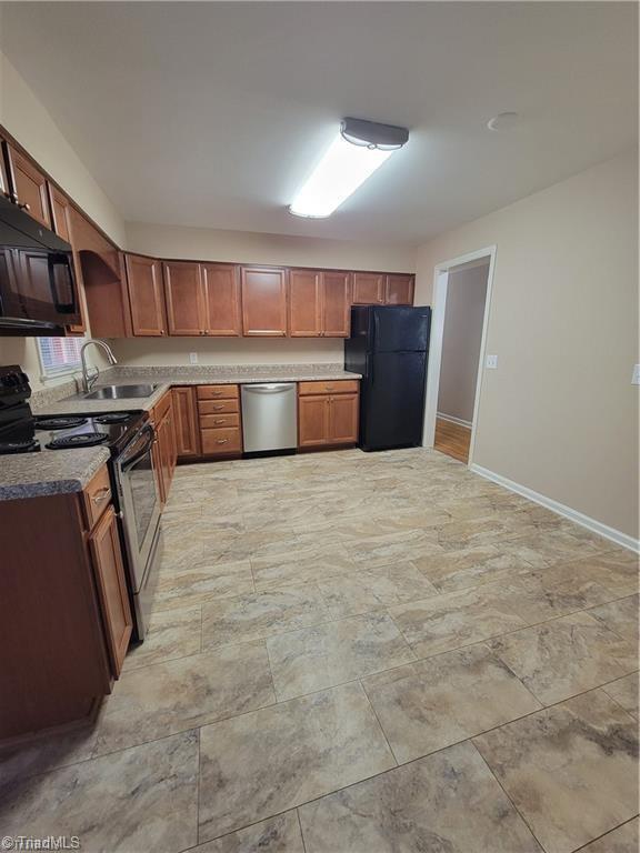 kitchen featuring black appliances, brown cabinetry, a sink, and baseboards