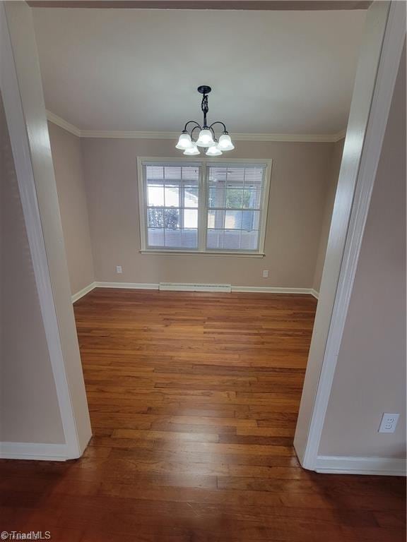 unfurnished dining area featuring an inviting chandelier, crown molding, baseboards, and wood finished floors