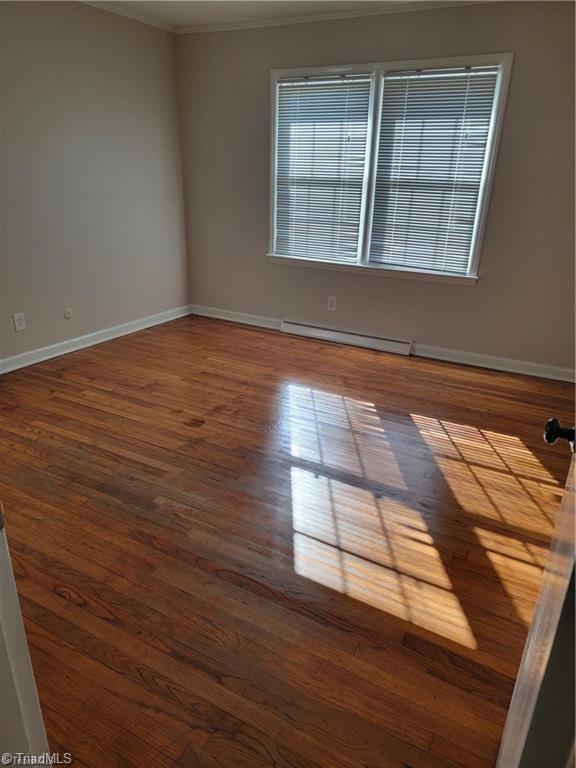 spare room featuring a baseboard radiator, crown molding, baseboards, and wood finished floors