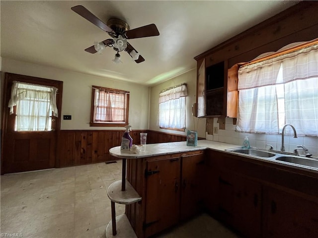 kitchen featuring kitchen peninsula, backsplash, ceiling fan, sink, and a breakfast bar area