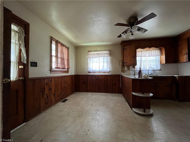 kitchen with ceiling fan, sink, wooden walls, kitchen peninsula, and decorative backsplash