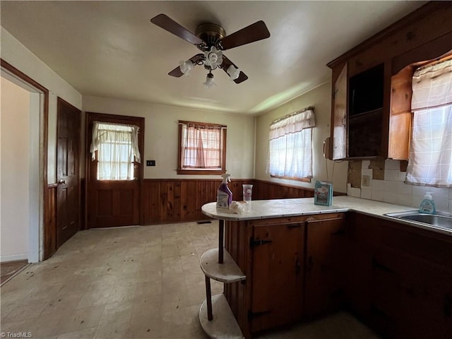 kitchen with kitchen peninsula, tasteful backsplash, a breakfast bar, ceiling fan, and wooden walls