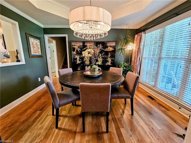 dining area featuring wood-type flooring, ornamental molding, and an inviting chandelier