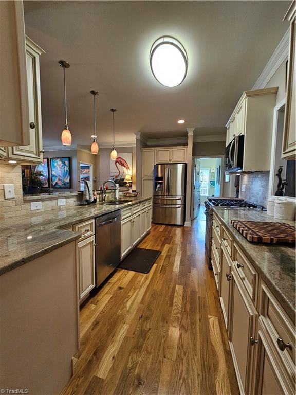 kitchen featuring hanging light fixtures, dark stone countertops, cream cabinets, wood-type flooring, and appliances with stainless steel finishes