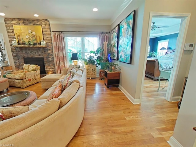 living room with a stone fireplace, ceiling fan, crown molding, and light hardwood / wood-style floors