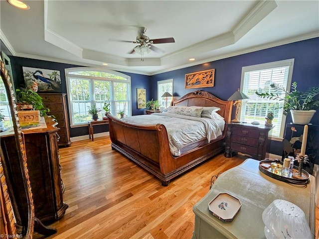 bedroom featuring ceiling fan, a raised ceiling, light wood-type flooring, and multiple windows