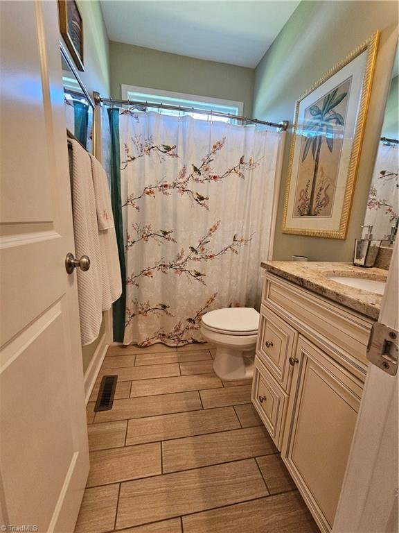 full bathroom with hardwood / wood-style floors, vanity, shower / tub combo, and toilet