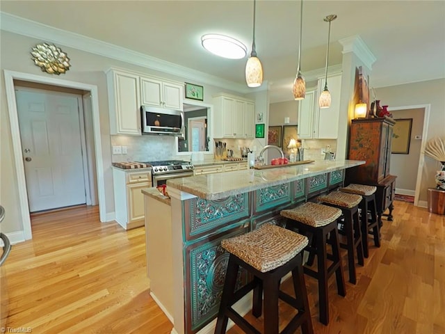 kitchen featuring kitchen peninsula, appliances with stainless steel finishes, backsplash, decorative light fixtures, and light hardwood / wood-style flooring