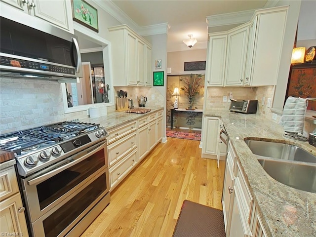 kitchen with light stone countertops, backsplash, appliances with stainless steel finishes, and light hardwood / wood-style flooring