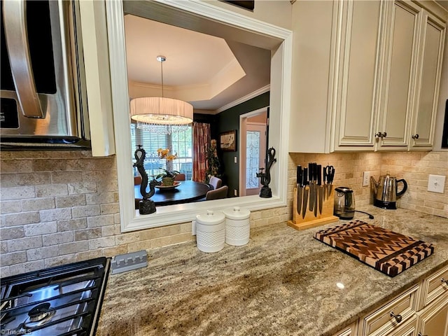 kitchen with ornamental molding, tasteful backsplash, cream cabinetry, decorative light fixtures, and light stone counters