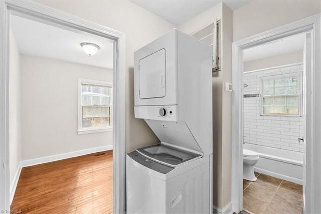 laundry area featuring hardwood / wood-style flooring, stacked washer and clothes dryer, and a wealth of natural light