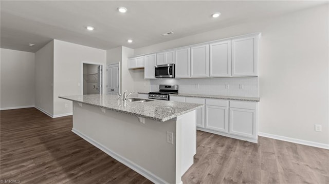 kitchen featuring stainless steel appliances, white cabinetry, light stone counters, and a center island with sink