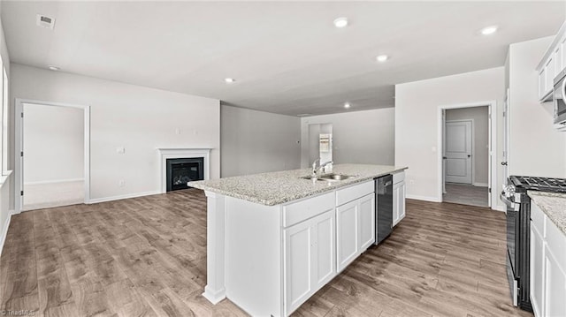 kitchen featuring sink, white cabinets, light stone counters, an island with sink, and stainless steel appliances