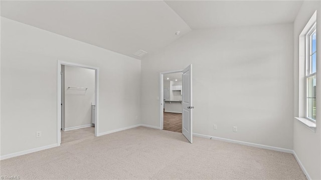 unfurnished bedroom with a walk in closet, light carpet, a closet, vaulted ceiling, and multiple windows