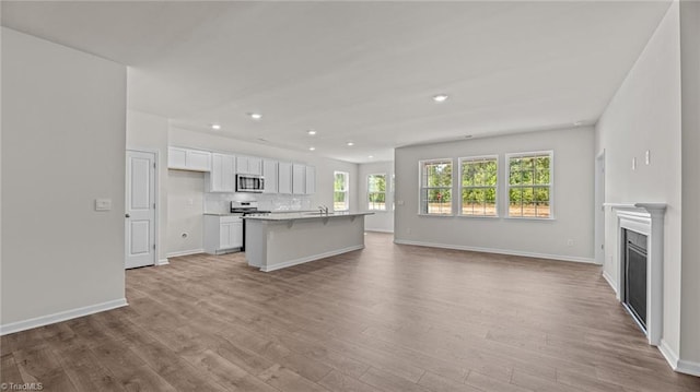 kitchen featuring white cabinets, appliances with stainless steel finishes, light hardwood / wood-style flooring, decorative backsplash, and a center island with sink