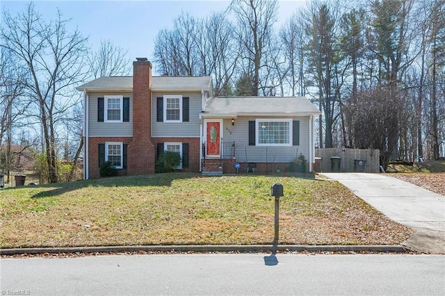 split level home featuring brick siding, a chimney, a front yard, and fence