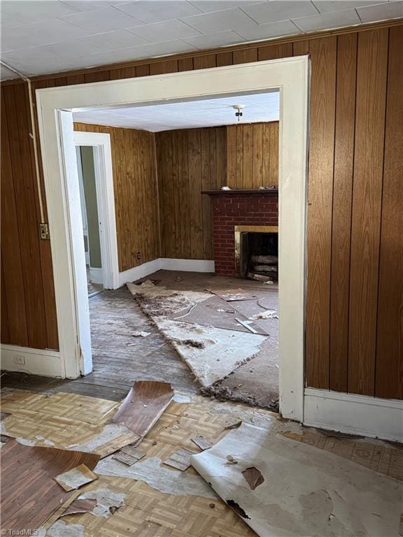 unfurnished living room featuring a brick fireplace and wooden walls