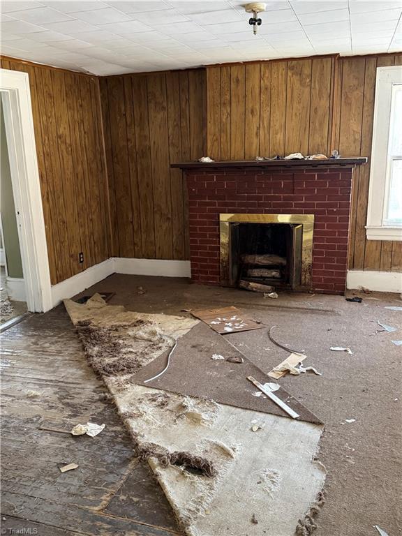 unfurnished living room featuring wooden walls and a brick fireplace