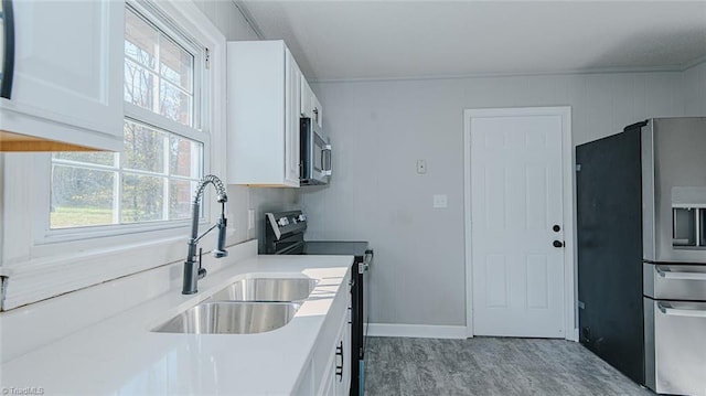 kitchen featuring white cabinetry, light wood-type flooring, ornamental molding, sink, and stainless steel appliances