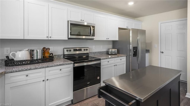 kitchen with light stone countertops, appliances with stainless steel finishes, white cabinets, and dark hardwood / wood-style flooring