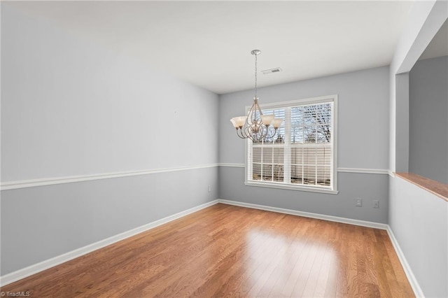 unfurnished dining area with a chandelier, baseboards, and wood finished floors