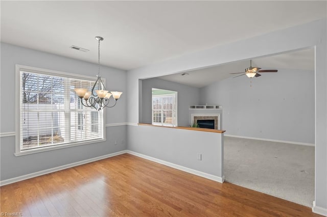 interior space featuring visible vents, baseboards, a tiled fireplace, vaulted ceiling, and wood finished floors