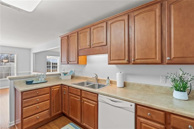 kitchen with dishwasher, light countertops, a peninsula, and a sink