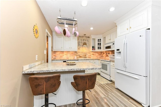 kitchen featuring a breakfast bar, white appliances, white cabinets, and tasteful backsplash