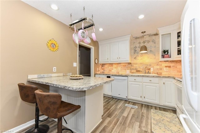 kitchen with pendant lighting, white appliances, white cabinets, kitchen peninsula, and a breakfast bar