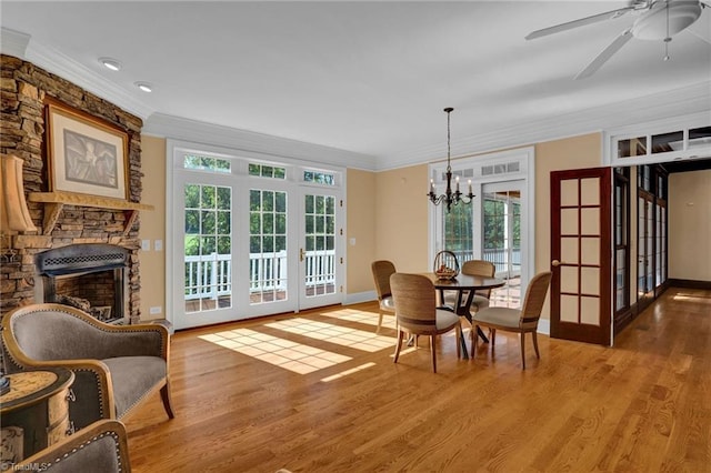 dining area featuring a stone fireplace, hardwood / wood-style flooring, ceiling fan with notable chandelier, and a healthy amount of sunlight