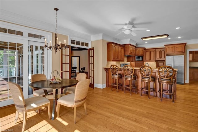 dining space with ceiling fan with notable chandelier, light wood-type flooring, and crown molding