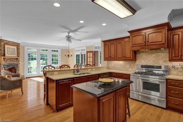 kitchen with light wood-type flooring, a kitchen breakfast bar, sink, stainless steel gas stove, and kitchen peninsula