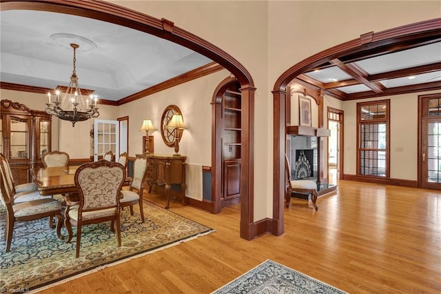 dining space featuring coffered ceiling, a chandelier, light hardwood / wood-style floors, and crown molding