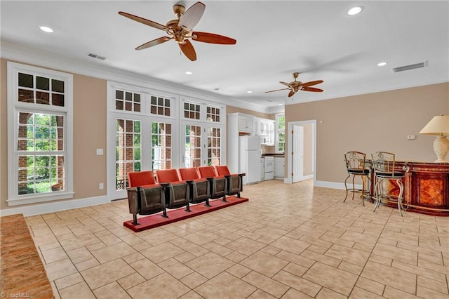 living area with baseboards, a ceiling fan, visible vents, and crown molding
