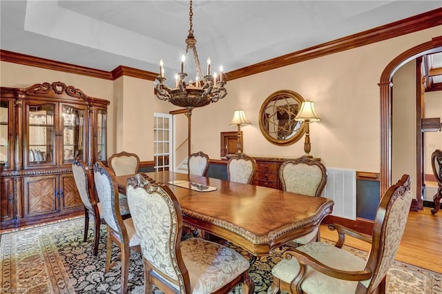 dining space featuring arched walkways, wood finished floors, ornamental molding, and a notable chandelier