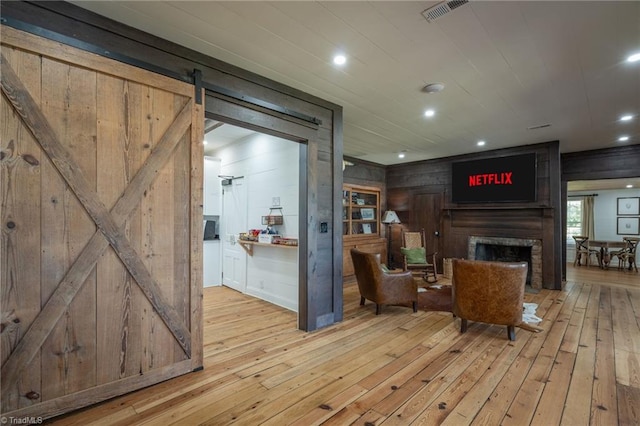 living room featuring a barn door, wooden walls, light wood-type flooring, a large fireplace, and visible vents