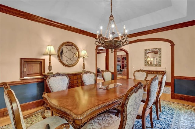 dining space with arched walkways, wood finished floors, crown molding, and an inviting chandelier