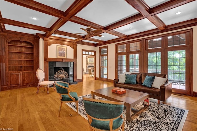 living room with beamed ceiling, light wood-style flooring, a fireplace with raised hearth, and ceiling fan