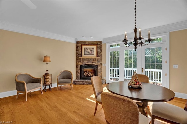 dining area with a stone fireplace, ornamental molding, light wood-style floors, baseboards, and a notable chandelier