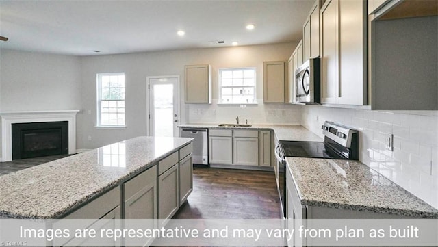 kitchen with a center island, light stone countertops, decorative backsplash, sink, and stainless steel appliances