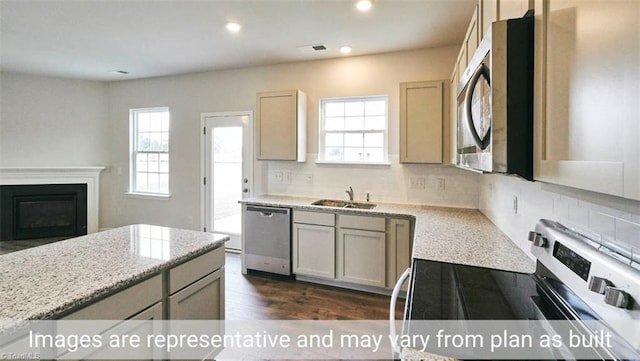 kitchen featuring appliances with stainless steel finishes, sink, dark wood-type flooring, light stone countertops, and decorative backsplash