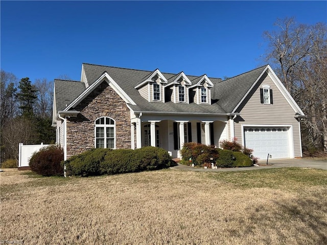 cape cod house featuring a porch, an attached garage, concrete driveway, a front lawn, and stone siding