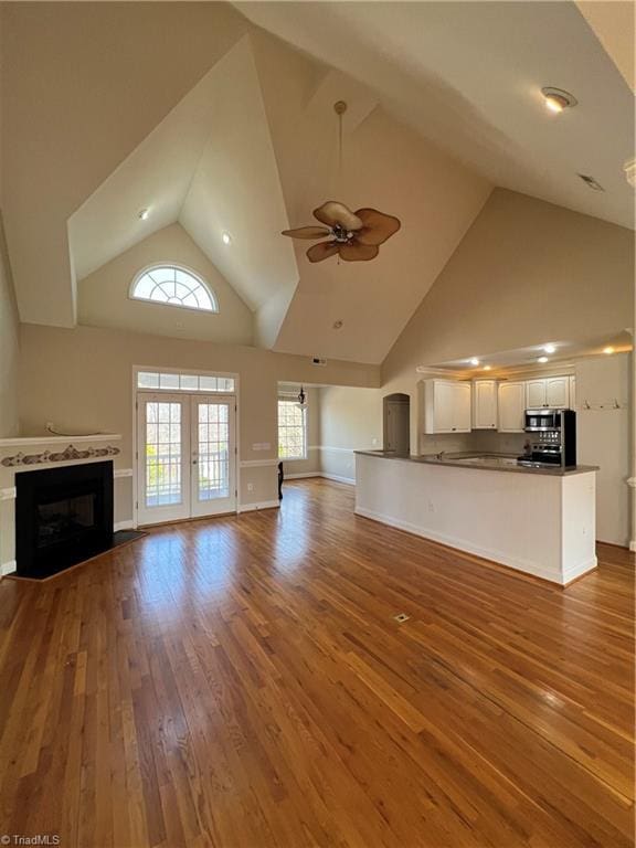 unfurnished living room featuring a fireplace with flush hearth, high vaulted ceiling, a ceiling fan, wood-type flooring, and baseboards