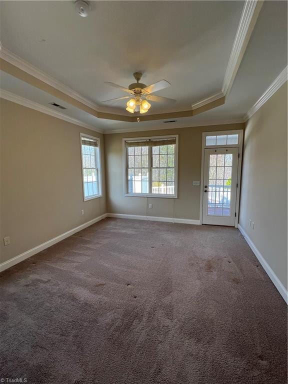 empty room featuring a raised ceiling, carpet, visible vents, and ceiling fan