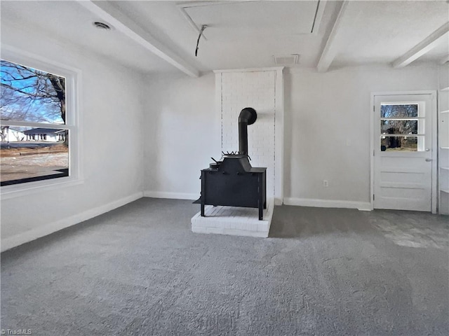 living room featuring dark colored carpet, beamed ceiling, and a wood stove