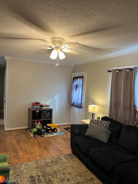 living area featuring baseboards, a ceiling fan, wood finished floors, crown molding, and a textured ceiling