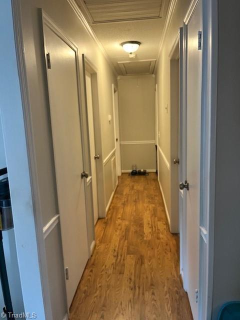 corridor featuring ornamental molding, attic access, and light wood-style floors